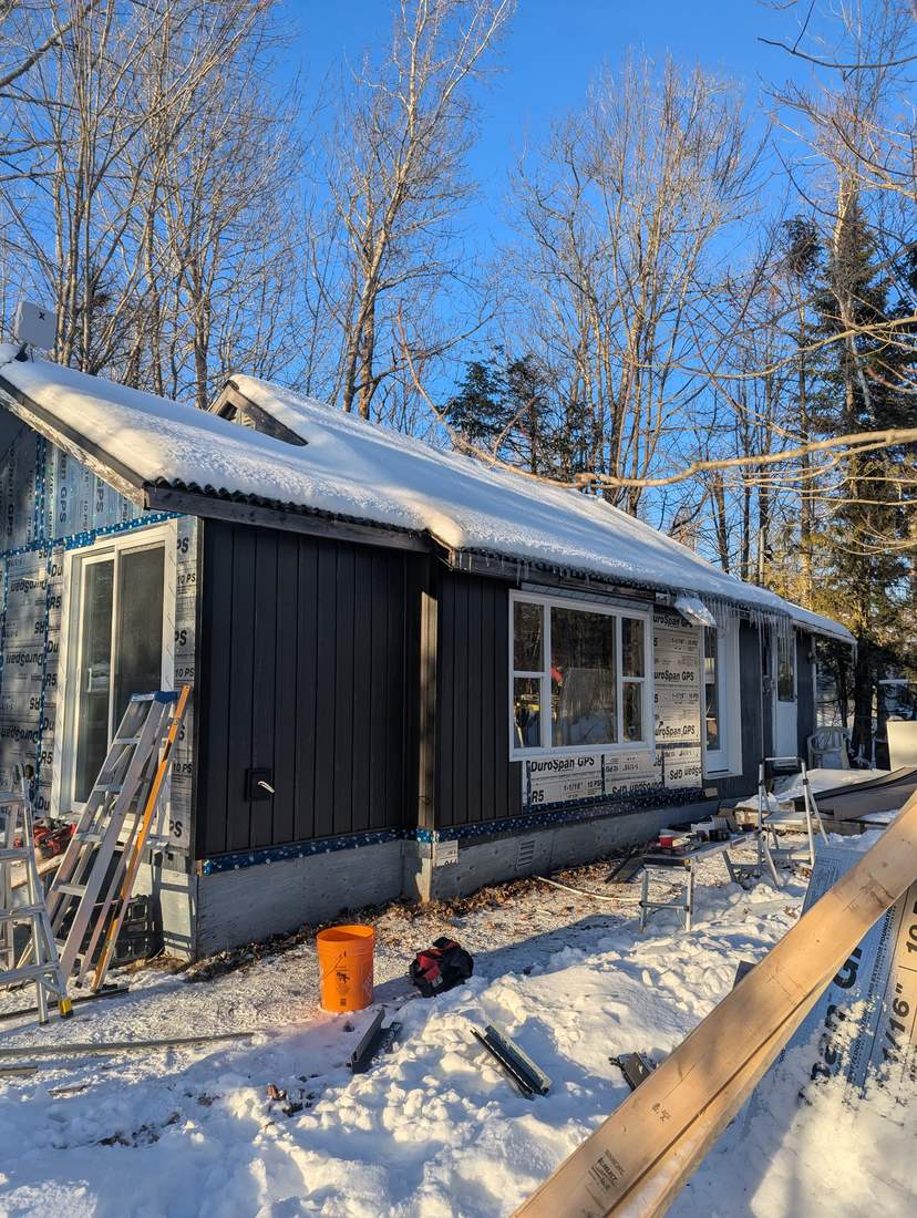 Black vertical board-and-batten steel siding partway through installation